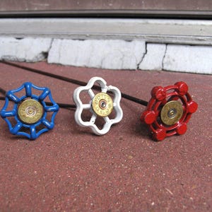 May include: Three decorative cabinet knobs in blue, white, and red. Each knob features a unique floral or geometric design with a brass center. The knobs are set against a red brick surface.