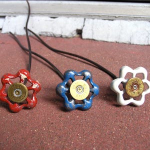 May include: Three metal valve handles in red, blue, and white, each featuring a brass-colored shotgun shell casing at the center. Each handle is attached to a thin, dark wire extending outward. The red and blue handles show signs of paint wear.