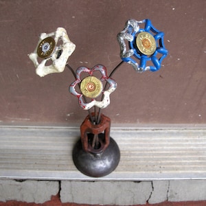 May include: A unique metal sculpture of three flower-like forms made from repurposed faucet handles and bullet casings. The handles are painted in white, red, and blue, with silver accents. The sculpture is mounted on a metal base.