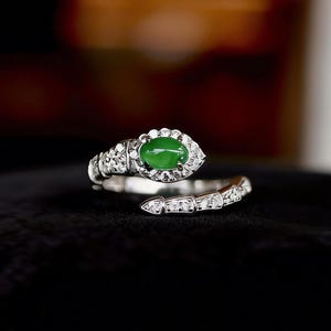 May include: A silver ring in a snake design, with a vivid green oval gemstone as the eye. The ring is embellished with small, sparkling white gemstones, giving a luxurious and elegant look. The snake's body coils around the finger, a unique piece of jewellery.