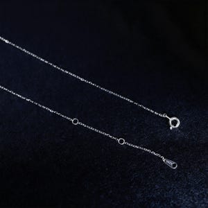 May include: A delicate silver necklace with a fine chain. The necklace features a small clasp and adjustable length with several small rings. The chain is displayed against a dark background.