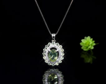 May include: A silver pendant necklace with a large oval-shaped, light green gemstone at the center, surrounded by smaller, round, light green stones. The necklace is on a black background with a flower.