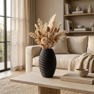 Puede incluir: Un jarrón negro mate con una textura acanalada en espiral contiene un gran arreglo de plantas secas de color beige, incluyendo hierba de la pampa, cápsulas de amapola y varios tallos plumosos, creando una composición de tonos neutros.