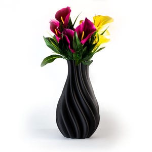 Puede incluir: Un jarr&oacute;n negro texturizado con un dise&ntilde;o en espiral contiene un ramo de flores coloridas. Las flores incluyen calas de color magenta oscuro y amarillo con follaje verde. El jarr&oacute;n est&aacute; sobre un fondo blanco.