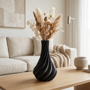 Puede incluir: Un jarrón negro mate con un diseño vertical en espiral y retorcido. El jarrón está lleno de un arreglo floral seco que presenta hierba de la pampa beige, vainas de semillas redondas y delicados tallos de lunaria translúcidos en tonos beige y crema.