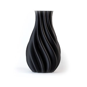 Puede incluir: Un jarr&oacute;n negro con un dise&ntilde;o &uacute;nico y ondulado. El jarr&oacute;n tiene una base ancha que se estrecha hacia un cuello m&aacute;s estrecho. La superficie tiene un acabado mate. El jarr&oacute;n es un art&iacute;culo decorativo para el hogar.