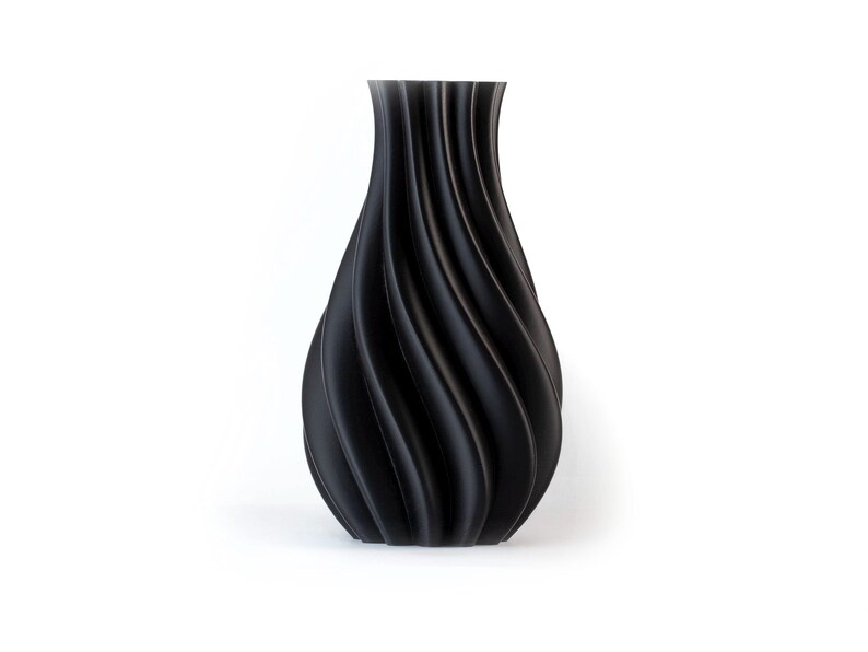 Puede incluir: Un jarr&oacute;n negro con un dise&ntilde;o &uacute;nico y ondulado. El jarr&oacute;n tiene una base ancha que se estrecha hacia un cuello m&aacute;s estrecho. La superficie tiene un acabado mate. El jarr&oacute;n es un art&iacute;culo decorativo para el hogar.