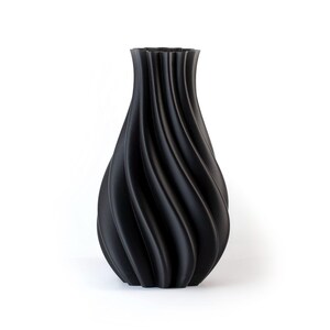 Puede incluir: Un jarr&oacute;n decorativo negro con un dise&ntilde;o &uacute;nico en espiral. El jarr&oacute;n tiene una base ancha que se estrecha hacia el cuello y una parte superior acampanada. La superficie tiene un acabado mate. El jarr&oacute;n es un art&iacute;culo de decoraci&oacute;n del hogar.