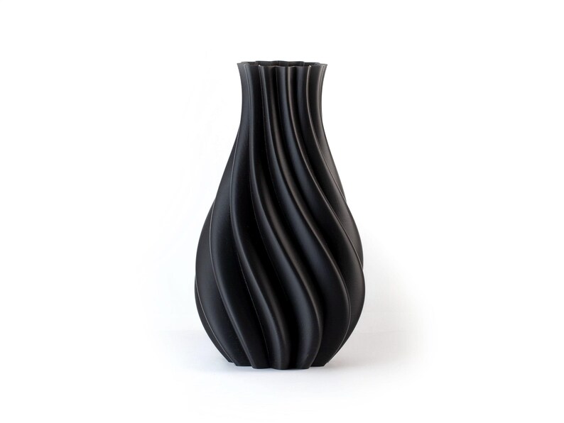 Puede incluir: Un jarr&oacute;n decorativo negro con un dise&ntilde;o &uacute;nico en espiral. El jarr&oacute;n tiene una base ancha que se estrecha hacia el cuello y una parte superior acampanada. La superficie tiene un acabado mate. El jarr&oacute;n es un art&iacute;culo de decoraci&oacute;n del hogar.