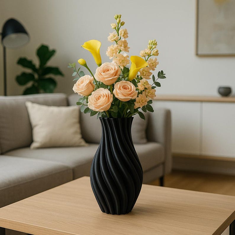 Puede incluir: Un jarr&oacute;n negro con textura en espiral contiene un ramo de rosas melocot&oacute;n, calas amarillas y flores melocot&oacute;n claro. El jarr&oacute;n est&aacute; sobre una mesa de madera clara, con un sof&aacute; gris y una l&aacute;mpara al fondo.