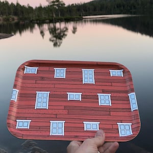 Könnte beinhalten: Ein rechteckiges Serviertablett mit einem roten Holzplanken-Design und weißen Fensterillustrationen. Das Tablett wird vor einer See- und Waldlandschaft mit einem rosa-blauen Himmel gehalten.