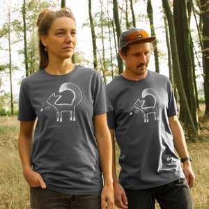 Könnte beinhalten: Zwei Personen tragen dunkelgraue T-Shirts mit einem weißen Aufdruck eines stilisierten Fuchses auf der Vorderseite. Der Fuchs schaut nach links und hat seinen Schwanz um seinen Körper gewickelt. Die Personen stehen in einem Wald.