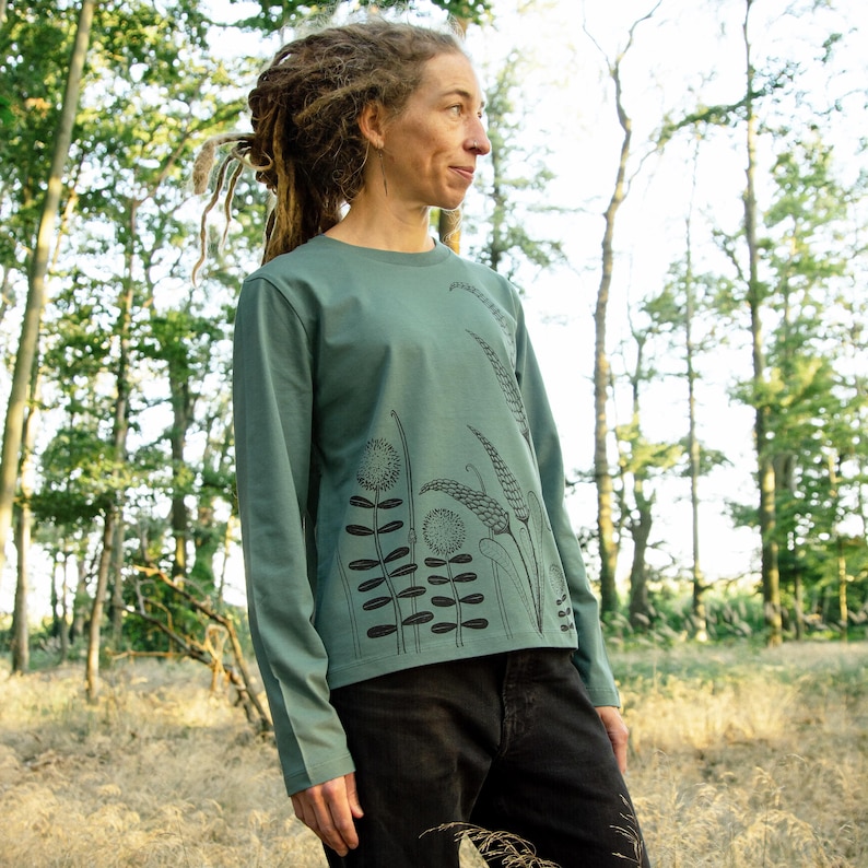 May include: A long-sleeved, teal green t-shirt with a black floral print. The print features stylised flowers and leaves.