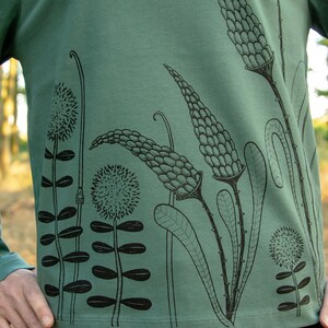 May include: A green long-sleeved shirt with a black floral print. The print features stylised flowers and leaves.