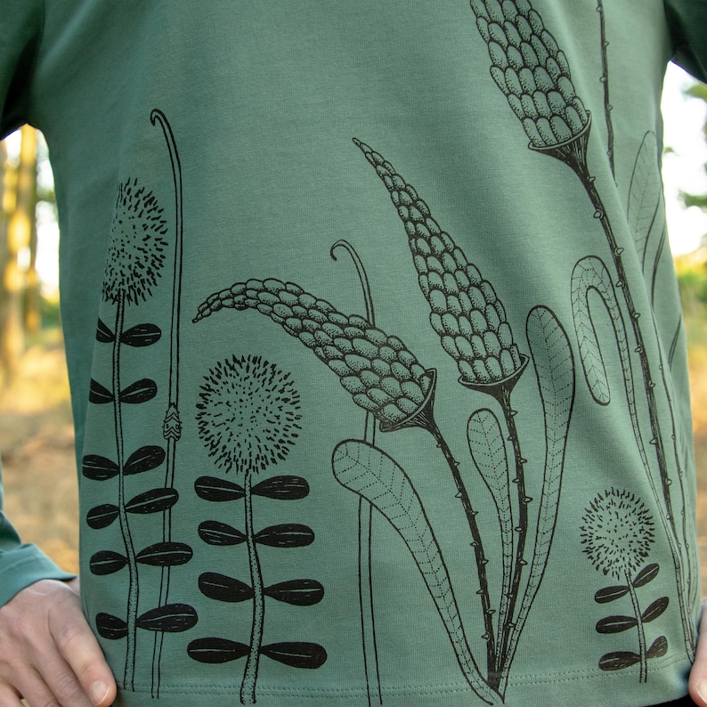 May include: A green long-sleeved shirt with a black floral print. The print features stylised flowers and leaves.