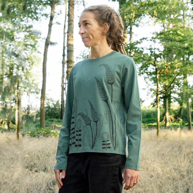 May include: A long-sleeved shirt with a green background and a black floral print. The shirt has a crew neck and a relaxed fit.