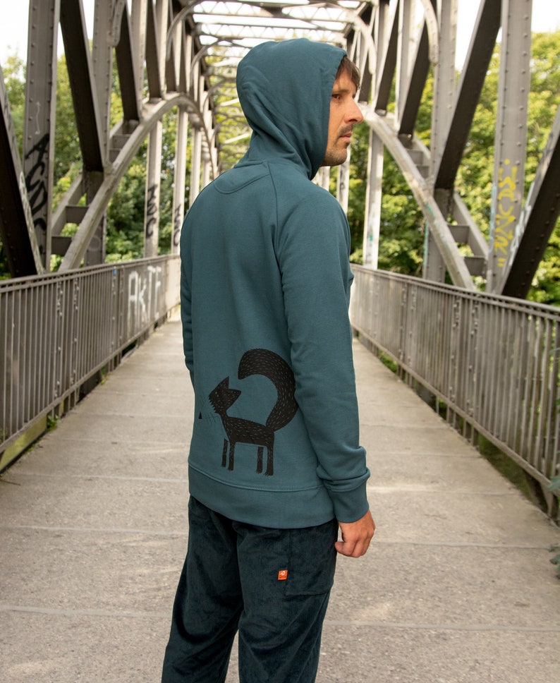 May include: A teal blue hooded sweatshirt with a black fox graphic on the back. The fox is stylized with a long, curled tail.