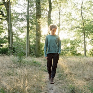 May include: A person wearing a teal long-sleeved shirt with a black graphic print of a forest scene and the word "Love" on it. The person is walking on a path in a forest.