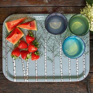 Peut inclure: Un plateau rectangulaire avec un motif de bouleaux, contenant des tranches de pastèque, des fraises et trois verres de boissons avec des tranches de citron. Le plateau est bleu clair avec un motif de bouleaux.