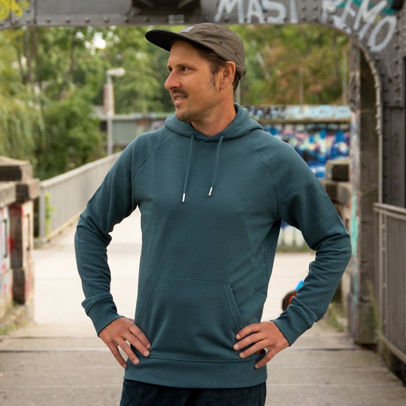 May include: A teal blue hooded sweatshirt with a kangaroo pocket. The sweatshirt has a relaxed fit and is made of a soft, comfortable fabric.