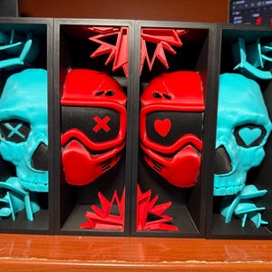 May include: A four-section display featuring teal skulls and red masks. The skulls have an X or heart in the eye sockets. The masks have an X or heart on the front. The display is black and sits on a brown surface.