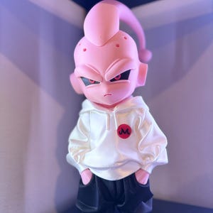 May include: A pink figurine of a character with an angry expression, wearing a white hoodie with a red "M" logo and black pants. The figure has a long, curved antenna and is standing with hands in pockets.