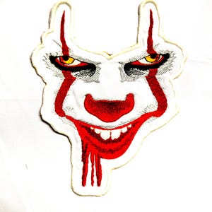 May include: Embroidered patch featuring a menacing clown face with red accents. The design includes a red nose, a wide, sinister grin, and red streaks. The eyes are yellow and the overall design is on a white background.