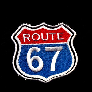 May include: Embroidered patch featuring the iconic Route 67 sign. The patch has a red top section with the word "ROUTE" in white, and a blue bottom section with the number "67" in white. The patch is bordered with white stitching.