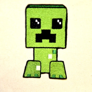 May include: A green embroidered patch featuring a pixelated Creeper character from the Minecraft video game. The Creeper has a square head, black eyes, and a black mouth. The patch is on a light-colored background.