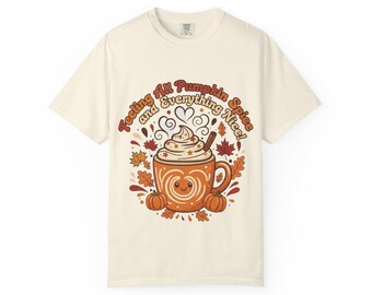 May include: Cream-colored t-shirt featuring a graphic of a smiling pumpkin spice latte with whipped cream, a cinnamon stick, and autumn leaves. The text "Feeling All Pumpkin Spice and Everything Nice!" is arched above the latte.