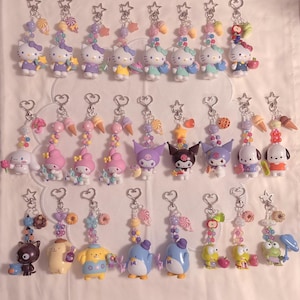 Peut inclure: Une collection de vingt-cinq porte-clés personnages représentant diverses figurines dont Hello Kitty, My Melody, Kuromi et d'autres. Chaque porte-clés comprend un fermoir en métal en forme d'étoile ou de cœur, des perles colorées et des breloques alimentaires.
