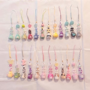 Puede incluir: Una colección de coloridos dijes de cuentas con varios diseños de animales y objetos. Los dijes presentan una variedad de colores, incluyendo rosa, azul, amarillo y morado. Cada dije está unido a un cordón fino a juego.