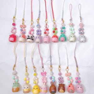 May include: A collection of colorful phone charms featuring various animal designs, including a panda, bear, and bunny. Each charm has a beaded accent and a cord for attaching to a phone or accessory. The charms are in shades of pink, purple, yellow, and brown.