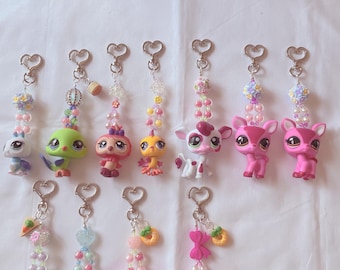 May include: Collection of colorful keychains featuring various animal figurines. Each keychain has a silver heart-shaped clasp and a beaded strand with decorative elements like flowers and charms. The animal figures include a bunny, koala, deer, and other creatures.