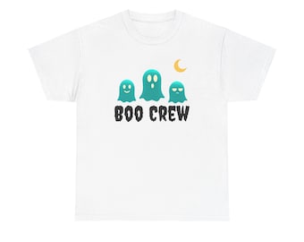 May include: A white short-sleeve t-shirt featuring a graphic of three teal ghosts with varying facial expressions positioned below a small yellow crescent moon. The text BOO CREW is printed in a black, distressed, jagged font below the ghosts.