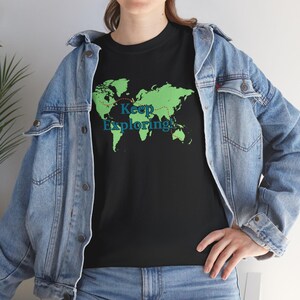 May include: Black t-shirt featuring a green world map design with a red dotted line and the words "Keep Exploring!" in teal. The shirt is worn with a blue denim jacket.