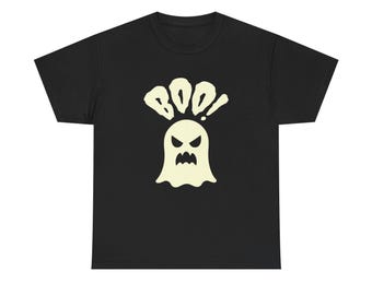 May include: A black short-sleeved t-shirt featuring a centered graphic of a pale yellow ghost with a jagged, angry expression. Above the ghost, the word BOO! is printed in a bold, stylized, pale yellow font that mimics a dripping or melting effect.