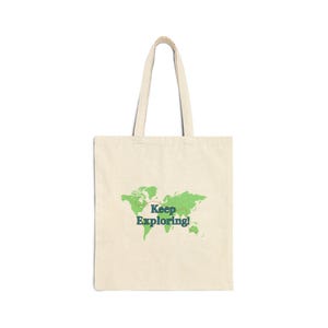 May include: Cream-colored tote bag with the words "Keep Exploring!" printed in blue and green over a green world map design. The bag has two handles and is made of a sturdy fabric.