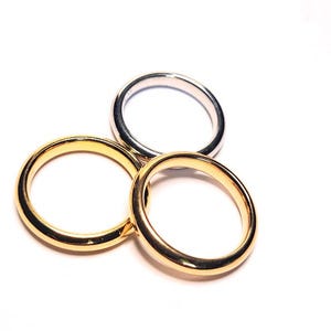 May include: A set of three plain, smooth metal rings arranged in a cluster. Two of the rings have a polished yellow gold finish, while the third ring features a bright, reflective silver-toned finish. Each band has a simple, rounded profile.
