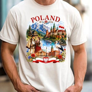 May include: An off-white t-shirt featuring a colorful graphic print with the text POLAND. The design includes a landscape with mountains, a castle, a stork, a couple in traditional attire, and a red and white ribbon with a white eagle emblem.