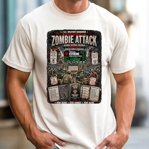Op de afbeelding: Ivoor kleurig t-shirt met een afbeelding uit het Amerikaanse militaire handboek over het overleven van een zombie-aanval. Het ontwerp bevat de tekst "ZOMBIE ATTACK" en "EXTREME" met verschillende verdedigingsstrategieën en waarschuwingen. Het shirt heeft ook de tekst "STAY ALERT STAY ARMED STAY ALIVE".