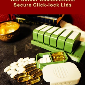 May include: A green pill organizer with five compartments and a white lid labeled Monday. The text 169 Colour Combinations Secure Click-lock Lids is visible. White oval tablets and yellow translucent gel capsules are arranged on the surface.