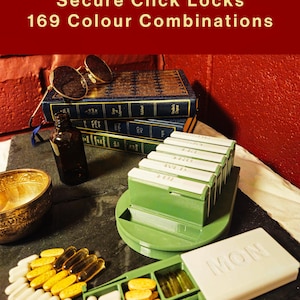 May include: A green weekly pill organizer with white lids labeled with days of the week, including a detached unit labeled MON. The text Secure Click Locks 169 Colour Combinations is visible. Various white and yellow capsules are scattered nearby.