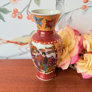 以下が含まれることがあります： フレアトップと丸いベースを備えた装飾的なセラミック花瓶。 花瓶は、花柄と風景のデザインを備えた赤と金の配色です。 花瓶の高さは約15cmです。