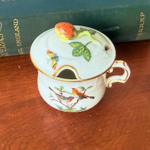 May include: White ceramic sugar bowl with a lid featuring a strawberry, butterfly, and leaf design. The bowl has a handle and is decorated with two birds on a branch. Gold trim accents the edges.