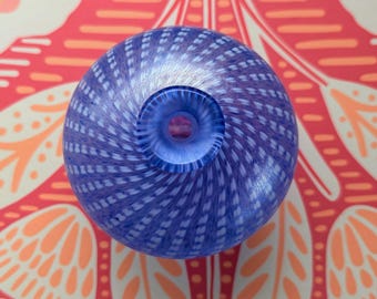 May include: A blue glass vase with a spiral pattern of white dots. The vase has a round shape with a small opening at the top. The background features a red and orange floral design.