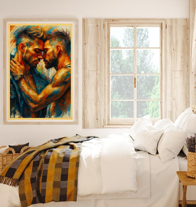 May include: An art print in a gold frame shows two men in an embrace, painted in blues, oranges, and yellows. The artwork hangs above a bed with white bedding, a plaid blanket, and a woven basket. A window with natural light is visible.