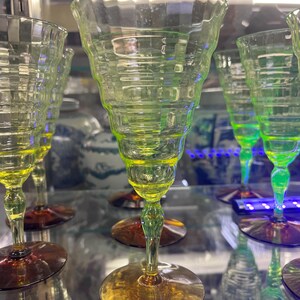 May include: A collection of vintage-style, stemmed glassware. The glasses feature a unique, textured design on the bowl and a gradient color scheme, transitioning from yellow to green. The base is a warm amber color.