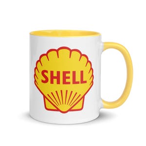 May include: White ceramic mug with a yellow interior and handle. The mug features the Shell logo, a yellow scallop shell with the word "SHELL" in red. The mug is designed for hot or cold beverages.