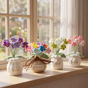 May include: Four crocheted flower arrangements in small pots sit on a windowsill. The flowers are various colors, including purple, pink, yellow, and white. The pots are white and beige, with small tags that read "handmade with love."